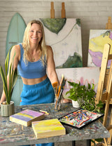 artist Skye Silver in her art studio standing in front of her abstract surf series paintings, with plants, easels, and art supplies on the table